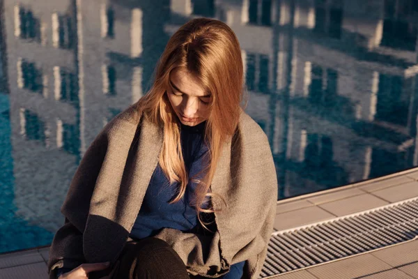 Élégante jeune fille blonde s'assoit près de la piscine bleue, se détend et se détend au soleil — Photo