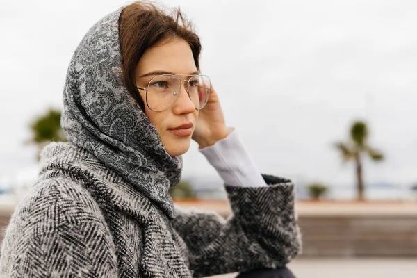 Elegante ragazza in un cappotto grigio e occhiali passeggiate al mare, in tempo nuvoloso — Foto Stock