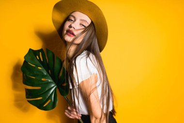 sarı arka plan üzerinde poz moda şapkalı çekici güzel uzun saçlı kız yaprak yeşil holding