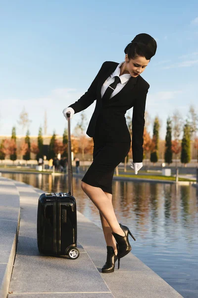 Vonzó fiatal nő stewardess egységes egy bőrönddel, séta a parkban — Stock Fotó