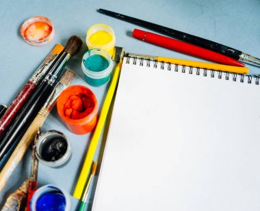 mavi bir masada sanatsal fırçaların, beyaz kağıt ve parlak renkler vardır