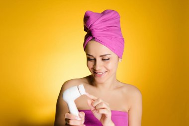 yüz cilt temizliği için elektrikli bir fırça tutan başında pembe havlu ile gülümseyen kız