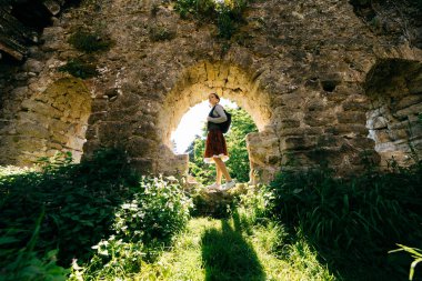yeşilliklerle çevrili bir eski yıkık binada duran genç bir kız dolaşıyor