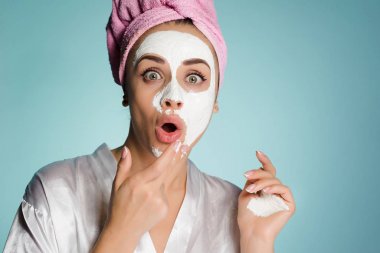 Kafasındaki bir havlu ile komik sürpriz kız nemlendirici maske yüzünde bir beyaz koyar