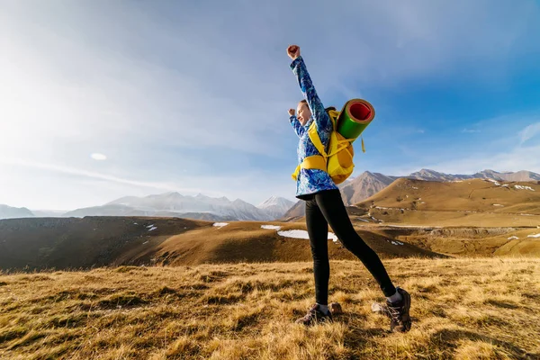 Felice ragazza attiva in una giacca blu viaggia attraverso le montagne del Caucaso con uno zaino, alzò le mani verso l'alto — Foto Stock