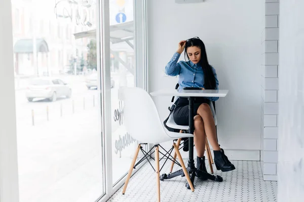Милая молодая девушка студентка в синей рубашке сидит в кафе после занятий в университете — стоковое фото