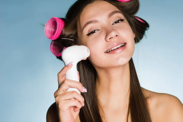 Gadis muda yang bahagia melakukan pembersihan mendalam dari kulit wajah dengan sikat listrik, di rambut keriting kepala — Stok Foto