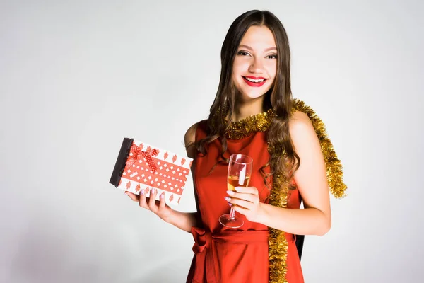 Happy beautiful girl in a red dress, with a gold tinsel around her neck, celebrating a new year, holding a glass with champagne — Stock Photo, Image