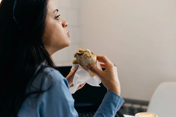 Mulher de negócios sentado no escritório na mesa e comer um sanduíche — Fotografia de Stock