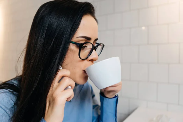 Žena sedí v kanceláři na stůl a pití kávy — Stock fotografie