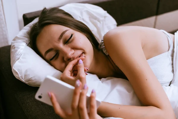 Wanita mengantuk berbaring di tempat tidur dan terlihat di telepon — Stok Foto