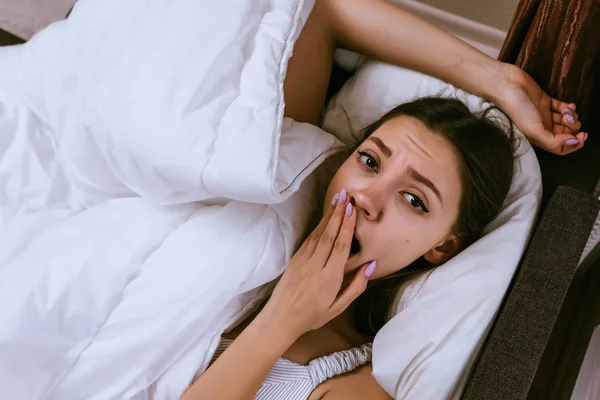 Mujer somnolienta yace en la cama y bosteza —  Fotos de Stock