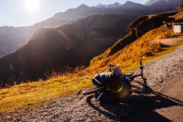 Una bicicletta con un grande zaino si trova sul lato della strada sullo sfondo delle montagne — Foto Stock