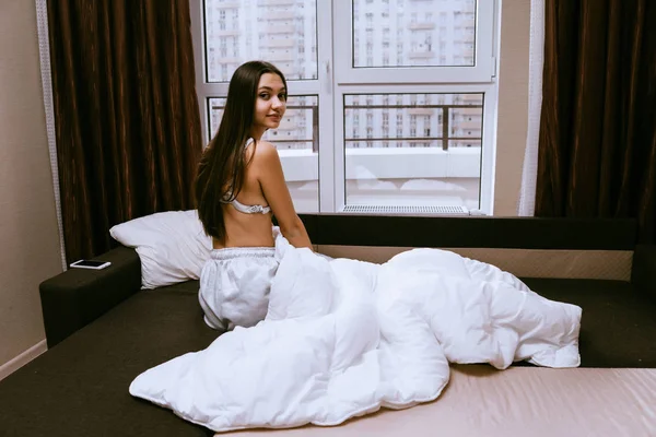 Женщина сидит на кровати на фоне большого окна — стоковое фото