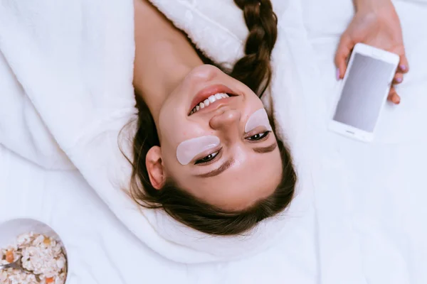 Gelukkige vrouw zetten patches onder de ogen en ligt op het bed — Stockfoto