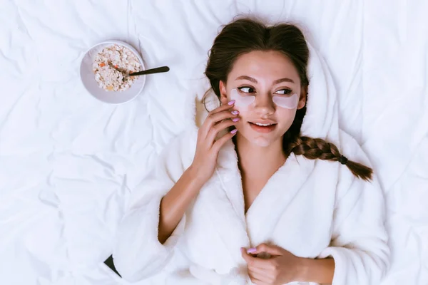 Una mujer puso parches bajo sus ojos y se acuesta en la cama —  Fotos de Stock