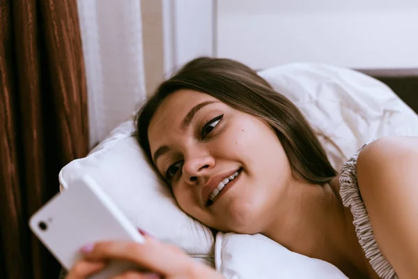 Wanita bahagia berbaring di tempat tidur dan memegang telepon di tangan — Stok Foto