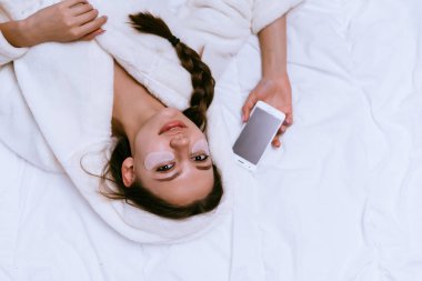 bir kadın gözleri altında yamalar koymak ve telefon elinde tutan