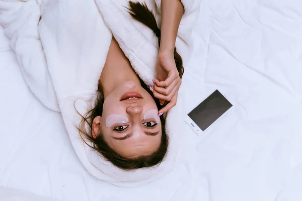 Женщина кладет пластыри под глаза и ложится на кровать — стоковое фото