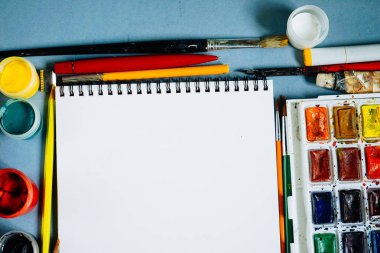 mavi bir arka plan üzerinde orada boyalar, fırçalar, kalem ve bir beyaz kağıt