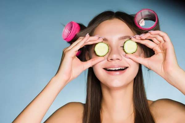 Žena na modrém pozadí se drží plátky okurky — Stock fotografie