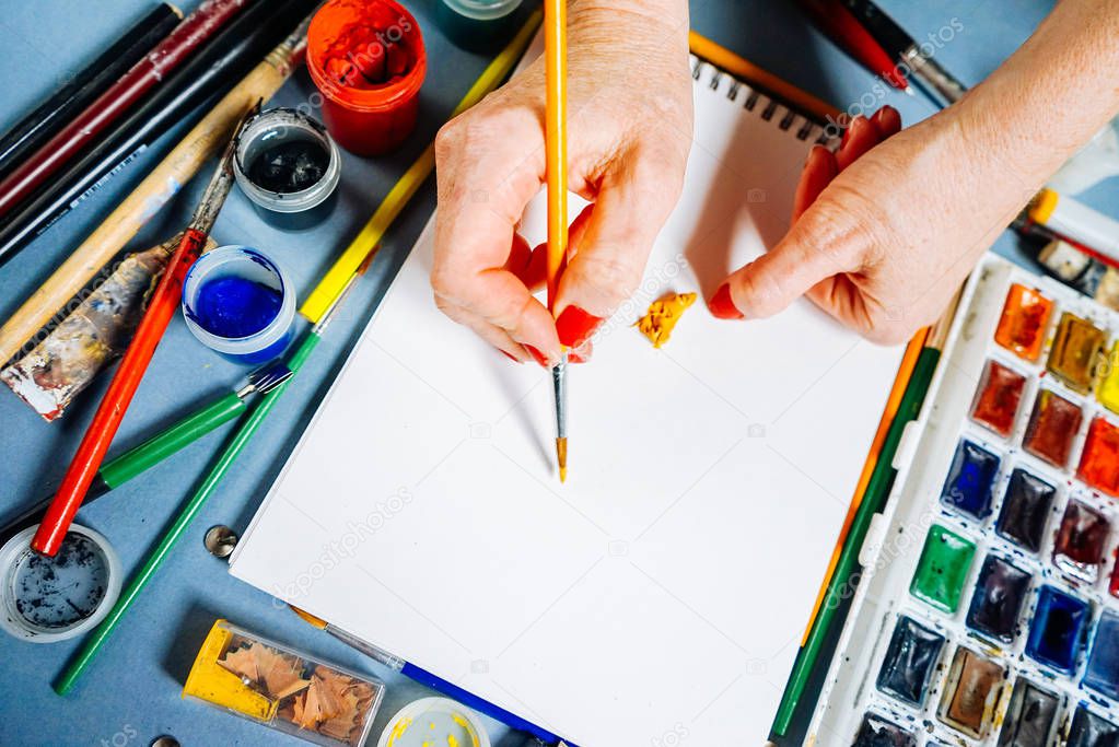 the artist draws on a white sheet of paper with colored paints