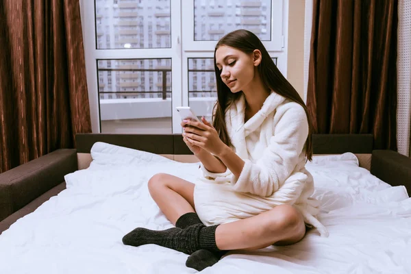 Vrouw is zittend op het bed en op zoek naar de telefoon — Stockfoto