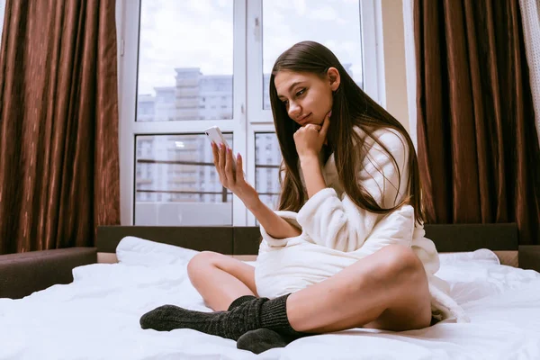 Mujer sentada en la cama en bata mirando el teléfono — Foto de Stock