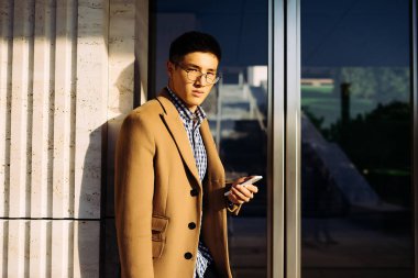 kahverengi ceketli genç bir adam bir telefon tutarak