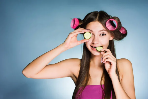 Kvinna med papiljotter på hennes huvud äta gurka — Stockfoto