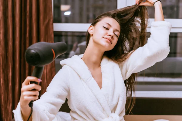 woman with long hair dries hair with a hairdryer