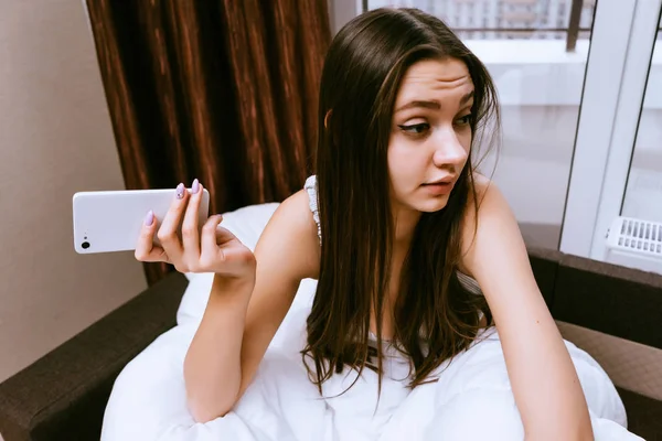 Terkejut wanita duduk di tempat tidur dengan telepon di tangan — Stok Foto