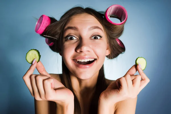 Lycklig kvinna med papiljotter på huvudet håller gurkor i hennes händer — Stockfoto