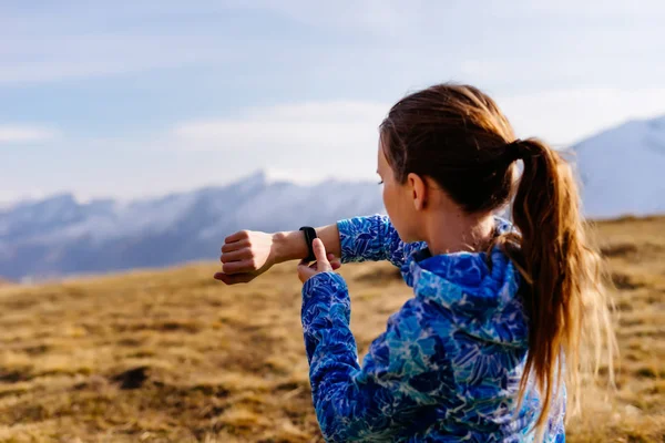 Kvinna turist tittar på fitness armband på bakgrund av berg — Stockfoto