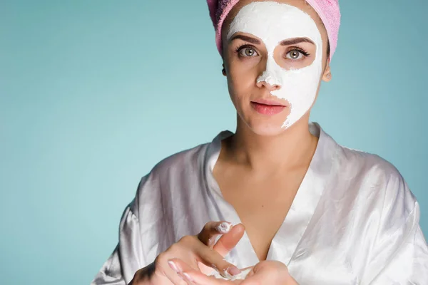 Egy zavarodott nő egy törülközővel, mint a fején tisztító maszk alkalmazni, az arcán — Stock Fotó