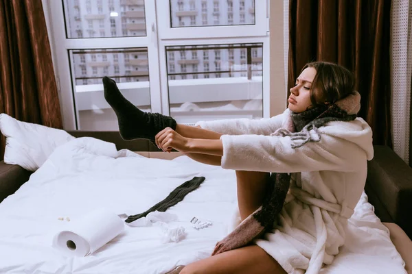 Μια άρρωστη γυναίκα κάθεται στο κρεβάτι και βάζει σε ζεστές κάλτσες — Φωτογραφία Αρχείου