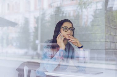 mavi tişört ve gözlük düşünceli genç kız bağımsız çalışma, telefonla pazarlık