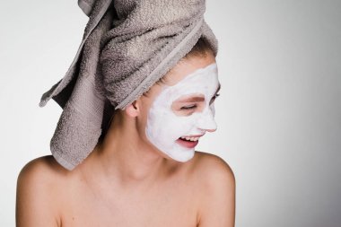 Kafasındaki gülüyor, nemlendirici maske onun yüz beyaz bir havlu ile genç mutlu kız