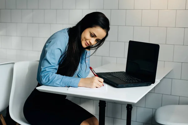 Счастливая женщина, сидящая за письменным столом в офисе и что-то пишущая — стоковое фото