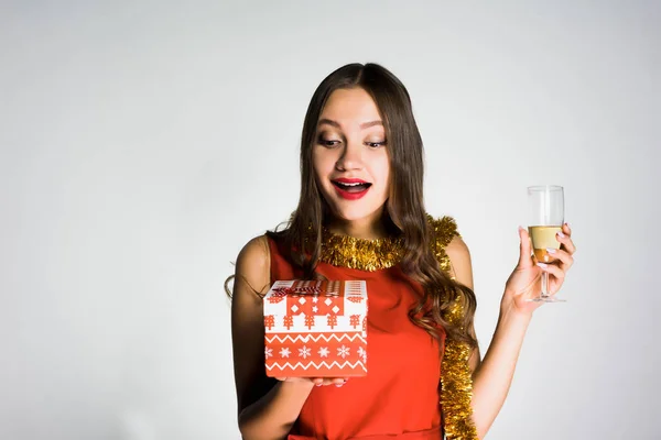 Glad ung flicka i röd klänning firar det nya året, håller ett glas champagne och en gåva — Stockfoto