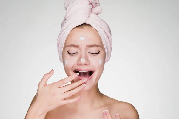 Young beautiful girl with a pink towel on her head applying moisturizer on her face — Stock Photo, Image