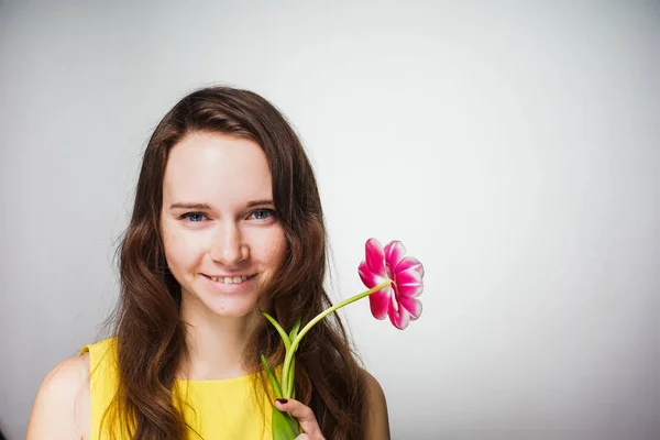 Glad vacker ung kvinna i gul klänning innehar rosa blomma, firar Mors dag — Stockfoto