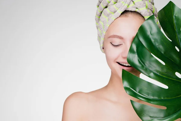 Gadis muda yang bahagia dengan handuk di kepalanya memegang daun hijau di tangannya, menikmati perawatan spa — Stok Foto