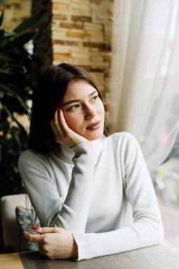 düşünceli pencereden dışarı bakarak bir kafede oturan genç güzel esmer kız