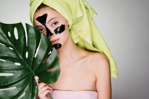 Una linda jovencita con una toalla verde en la cabeza se aplicó una máscara negra en las zonas problemáticas de su cara — Foto de Stock