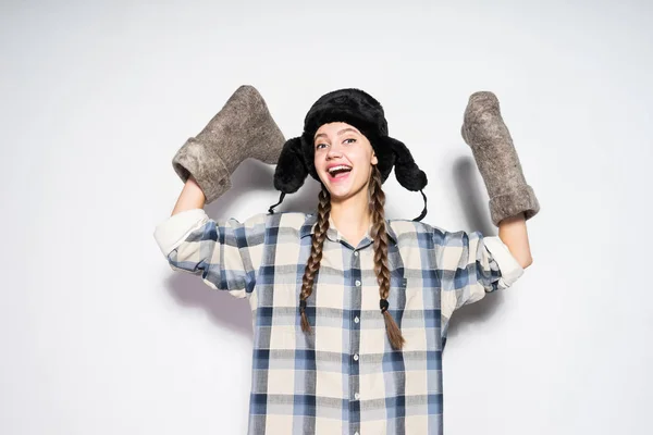 Счастливая смеющаяся русская девушка в теплой шляпе держит зимние войлочные сапоги — стоковое фото