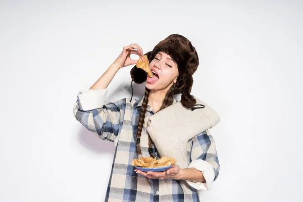 Kürk şapka içinde genç bir Rus kız sıcak lezzetli gözleme, Shrovetide kutluyor yiyor — Stok fotoğraf