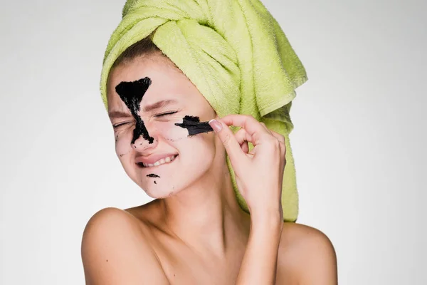 Незадоволена молода дівчина з зеленим рушником на голові видаляє чорну маску з її обличчя, це болить її — стокове фото