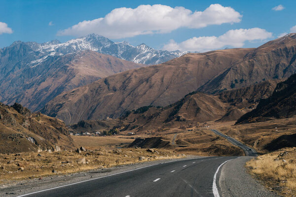 шоссе у подножия высоких гор, величественная природа, холмы и склоны покрыты белым снегом
