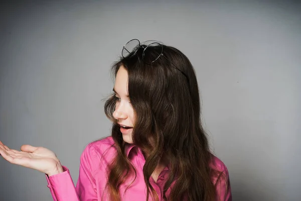 Hermosa joven con una camisa rosa, con el pelo largo, muestra algo a mano — Foto de Stock